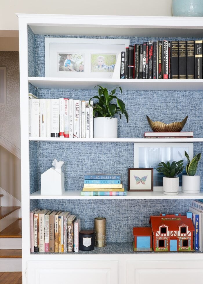 Blue peel and stick wallpaper on back on white bookcase styled with books and accessories