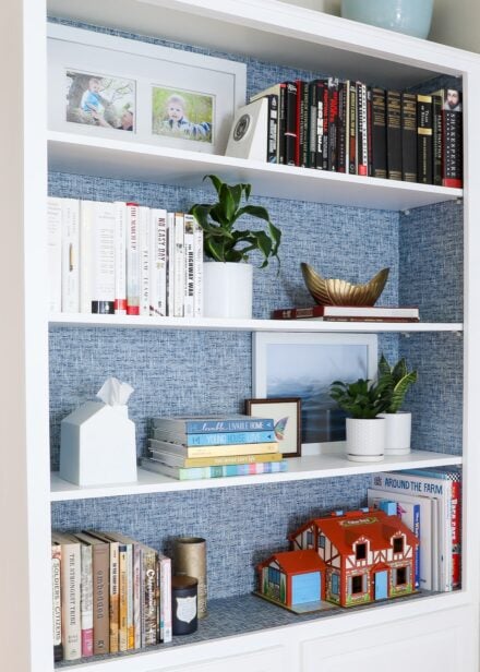 Blue peel and stick wallpaper on back on white bookcase styled with books and accessories