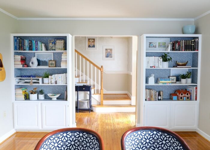 Built-in bookcases on either side of cased opening in family room with blue wallpaper backing