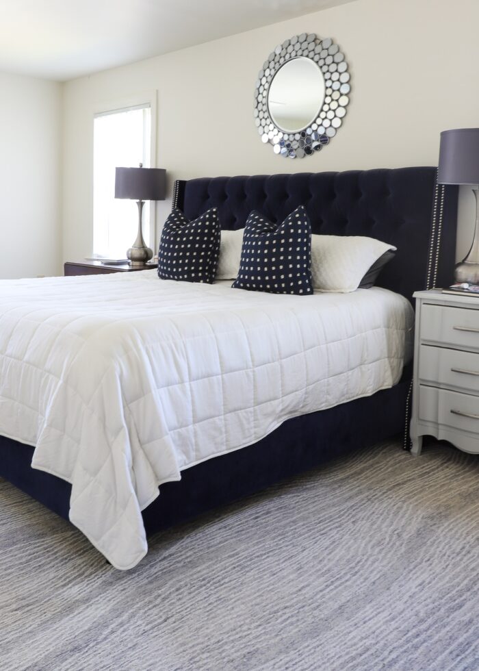 Navy velvet bed on grey rug with grey lamps and grey mirror