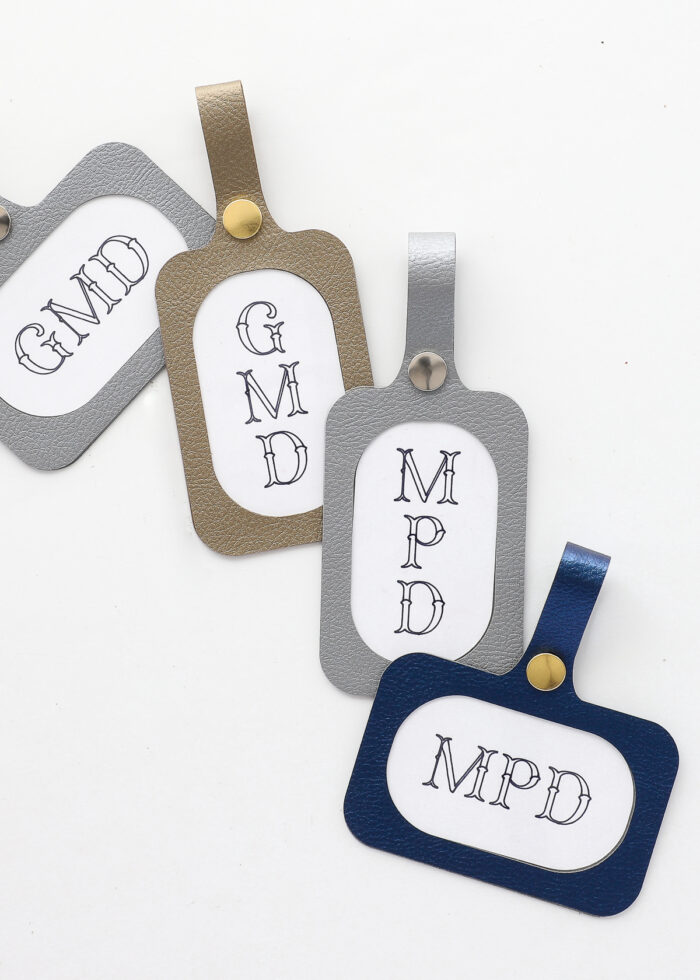Four luggage tags made with a Cricut using faux leather with printed monogram labels on a white table surface