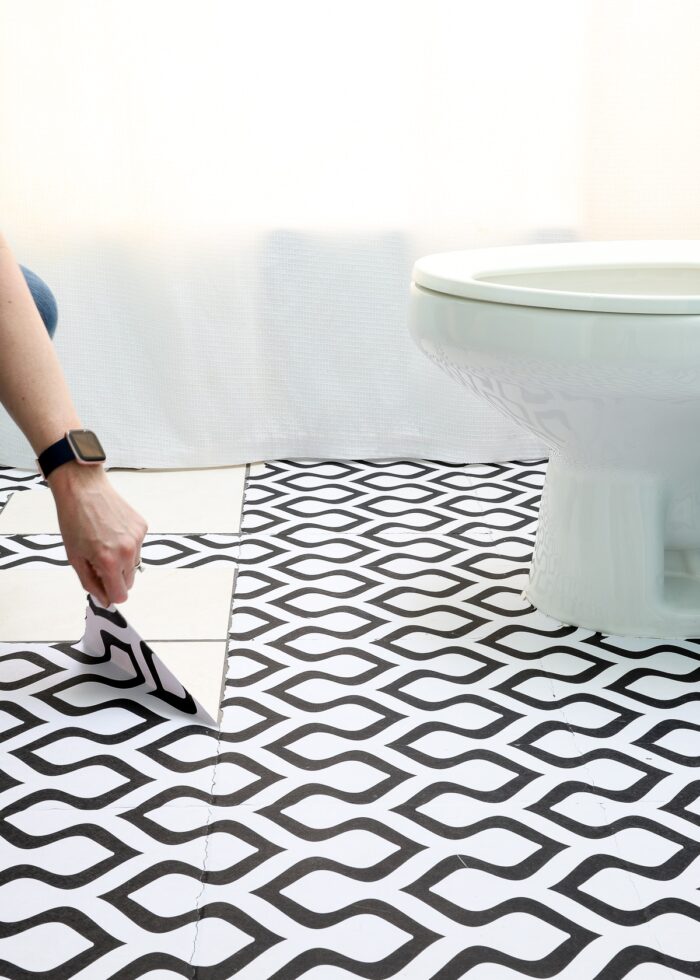 Hand peeling up wallpaper on a bathroom tile floor