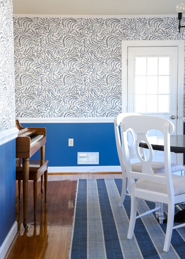 Formal dining room with blue and white wallpaper above chair rail and blue paint below