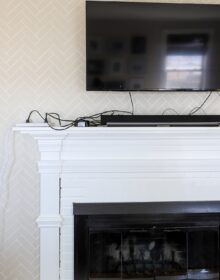 TV mounted above a white fireplace mantel with a mess of cords showing