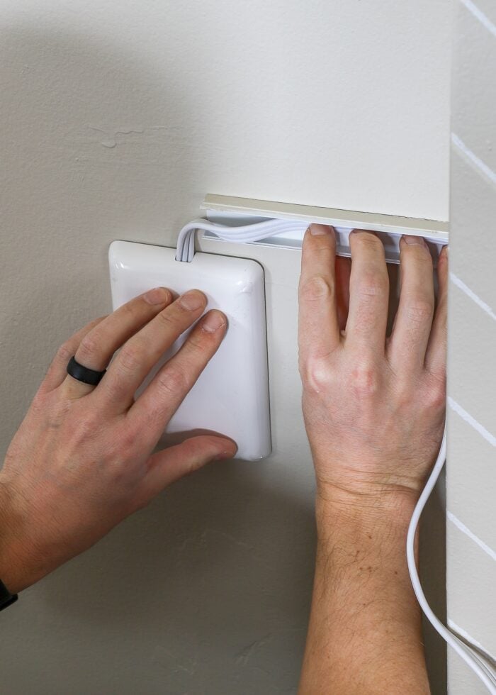 Hands putting cord into wall-mounted cord concealer
