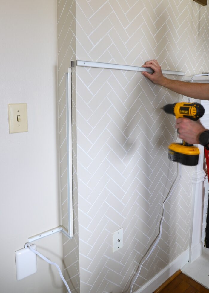 Hands drilling a corn conceal track to a beige wall