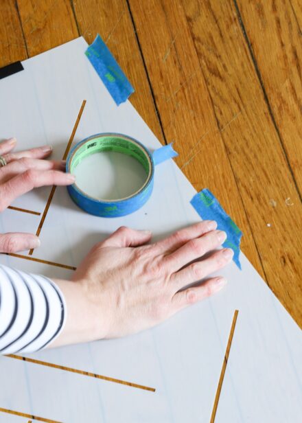 Hands placing painter's tape onto a wall stencil