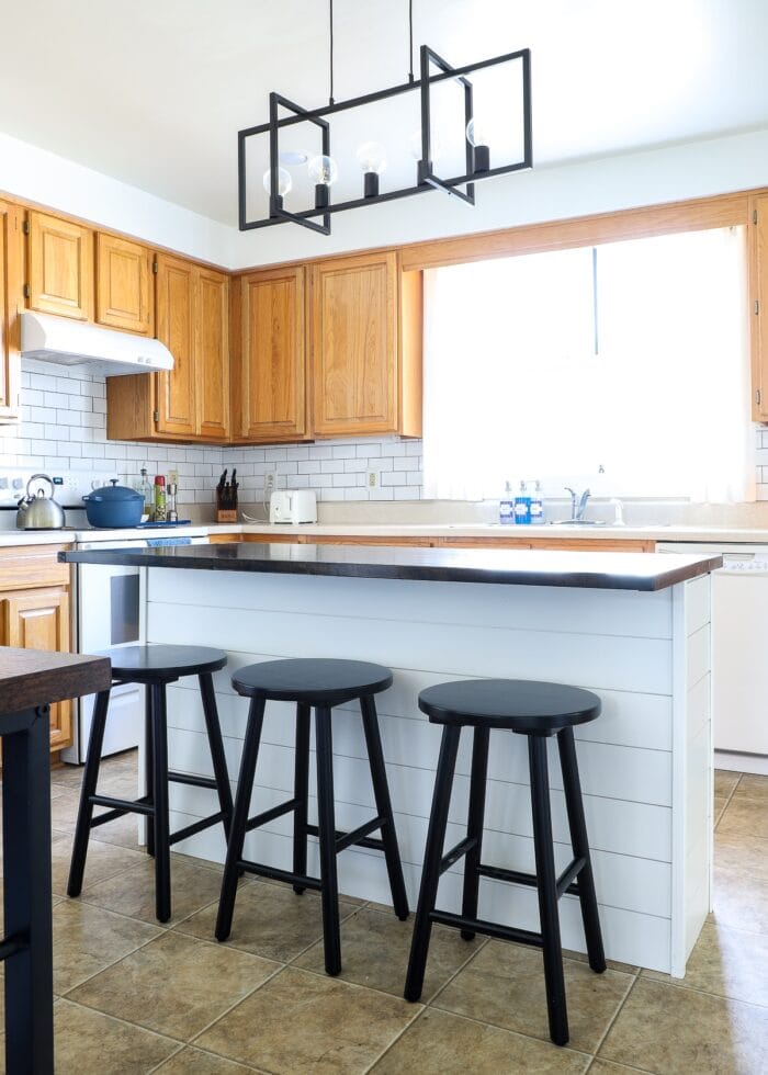 White shiplap on a kitchen island with a dark wood topper and black stools in an oak rental kitchen