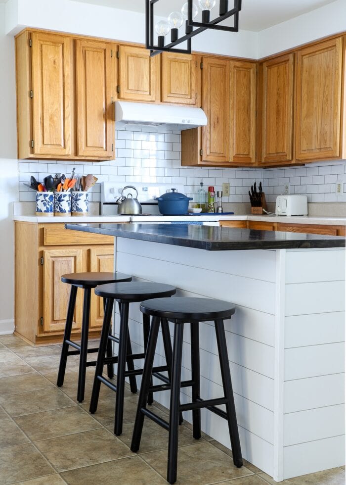 White shiplap on a kitchen island with a dark wood topper and black stools in an oak rental kitchen