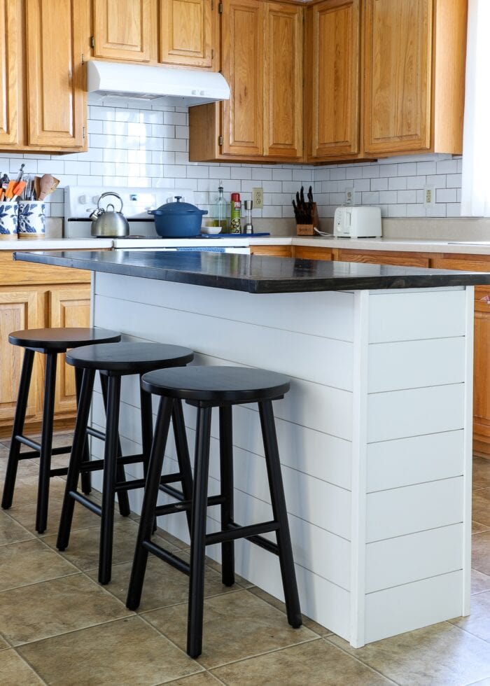 White shiplap on a kitchen island with a dark wood topper and black stools