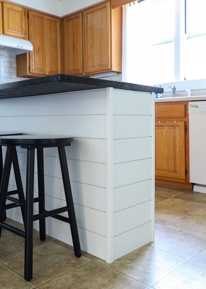 White shiplap on a kitchen island with a dark wood topper and black stools