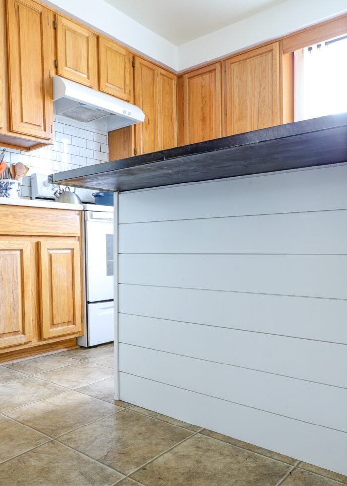 Kitchen island covered in white shiplap with dark countertop