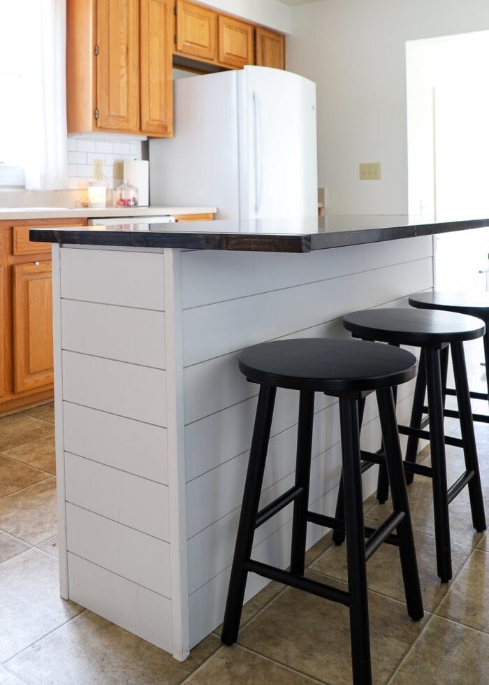 White shiplap on a kitchen island with a dark butcher block wood topper and black stools