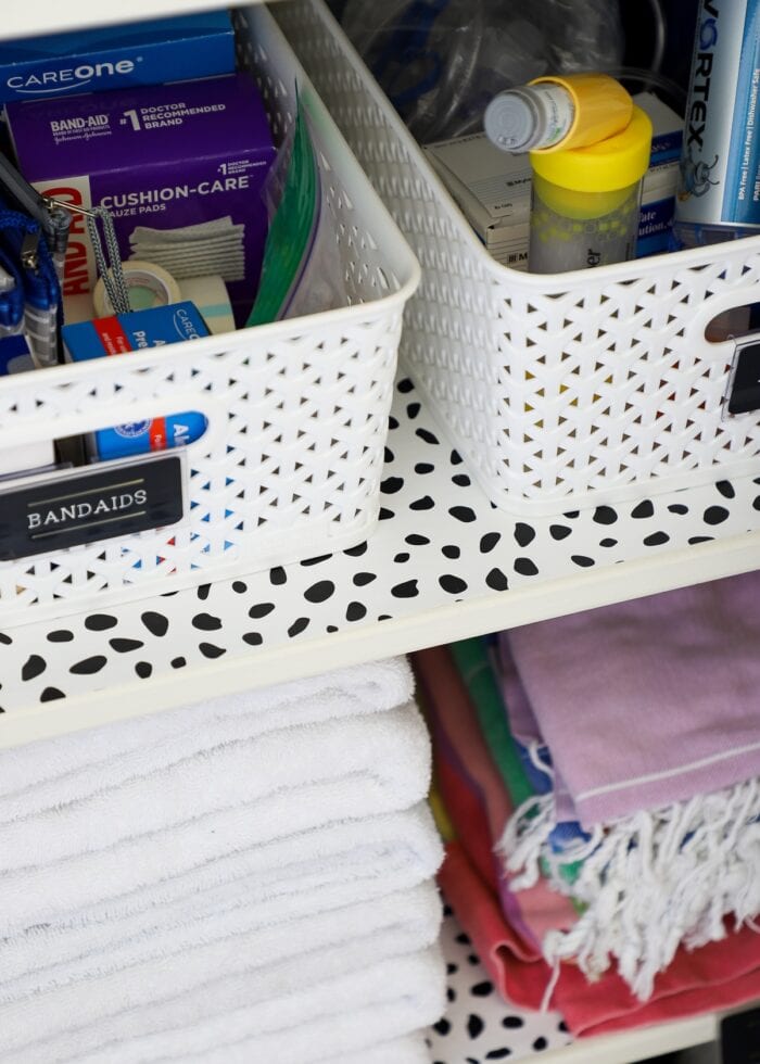 Black and white dotted shelf liner on an organized bathroom closet shelf
