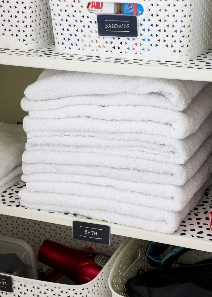 A stack of folded white towels on a bathroom closet shelf