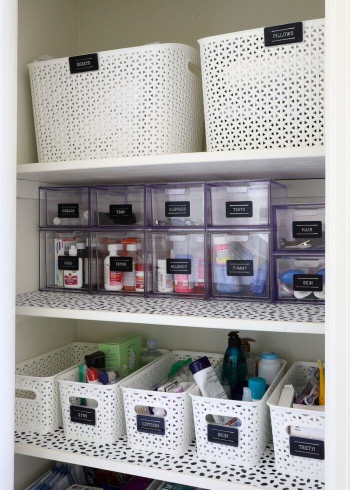 Clear acrylic drawers and white baskets used to organize bathroom closet shelves