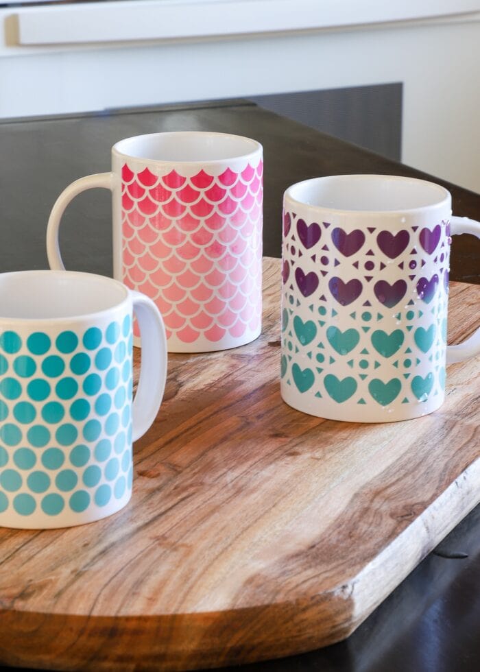 Three white mugs on a wooden cutting board with patterns made from Cricut Color Changing Vinyl