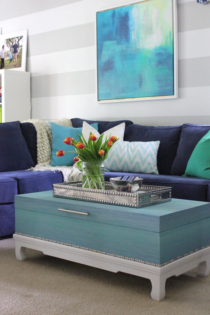 Grey striped living room with blue couch and turquoise trunk coffee table