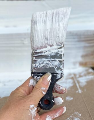 Hand holding a paint brush with white paint on it