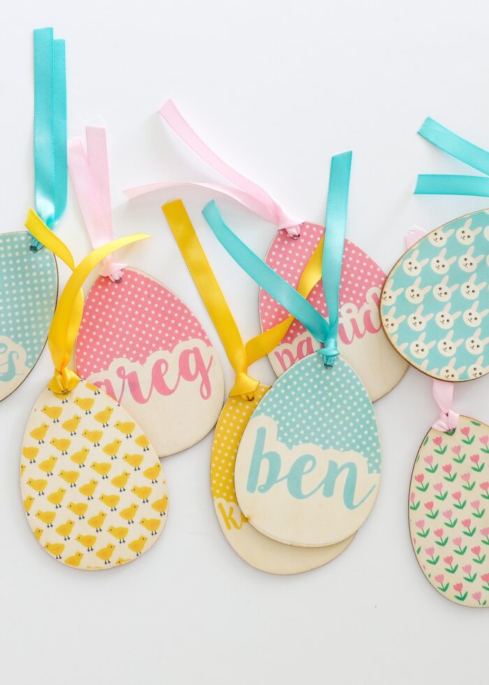 Pink, blue, and yellow personalized wooden egg-shaped Easter basket name tags made with heat transfer paper