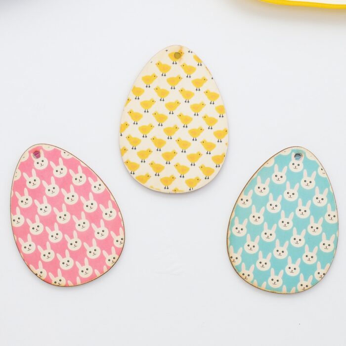Pink, blue, and yellow wooden egg-shaped Easter basket name tags made with heat transfer paper