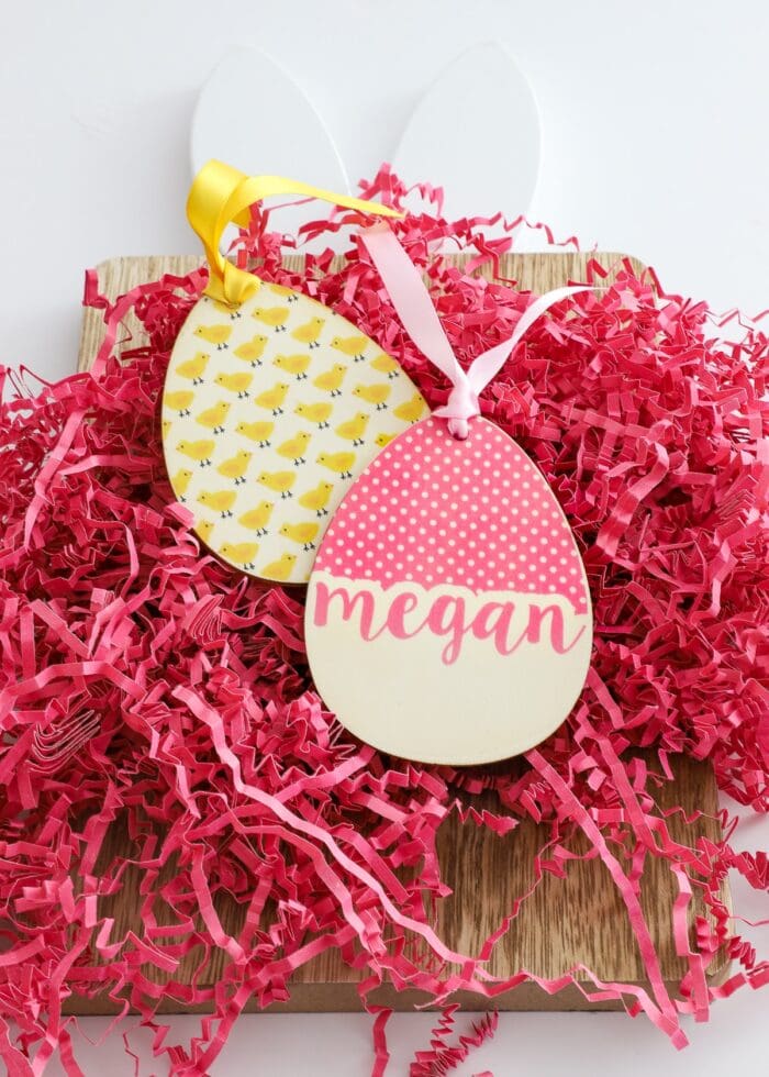 Wooden egg-shaped easter basket name tags in pink and yellow on pink paper grass