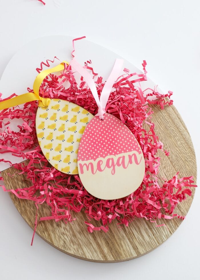 Wooden egg-shaped easter basket name tags in pink and yellow on pink paper grass