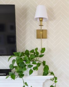 Wireless brass wall sconce above a white mantel and a plant