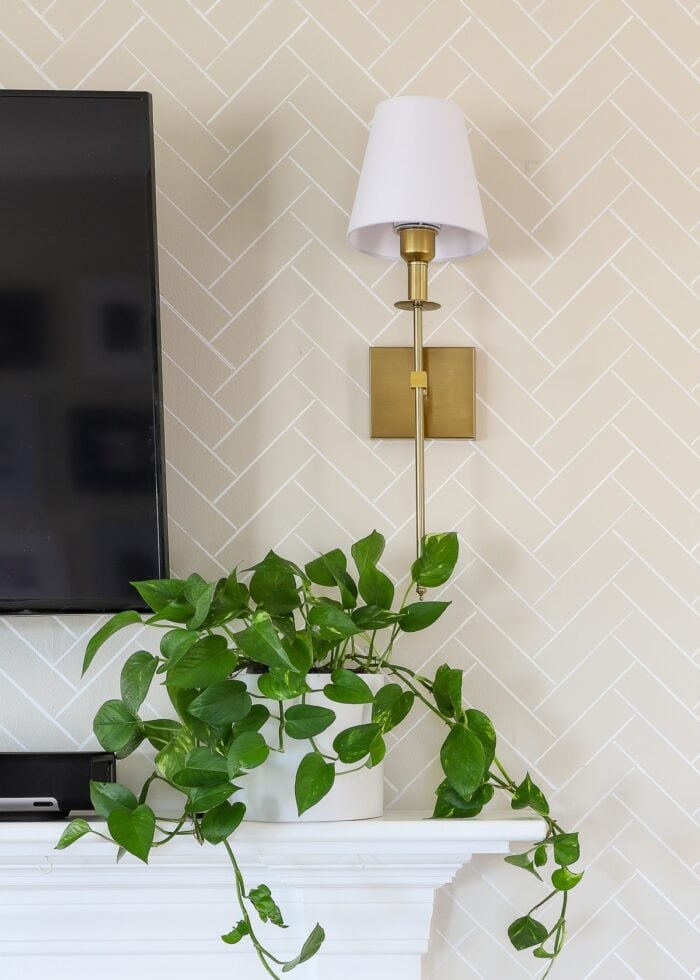 Wireless brass wall sconce above a white mantel and a plant on rental walls