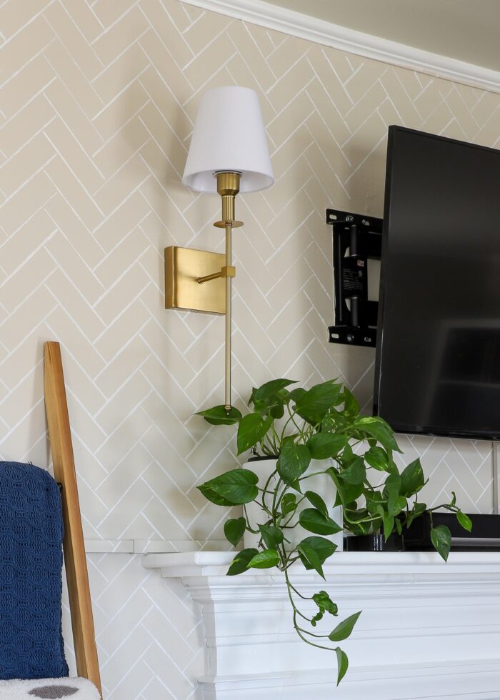 Brass wall sconce hung on a beige stenciled wall above a mantel