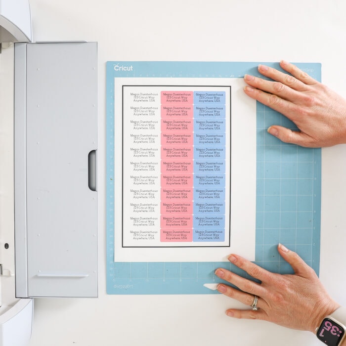 Hands placing printed Return Address Labels onto blue Cricut mat