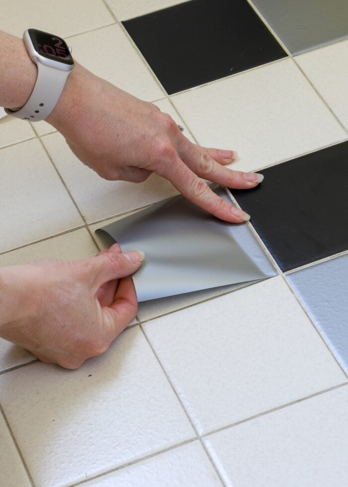 Hands placing vinyl square onto bathroom tile floor