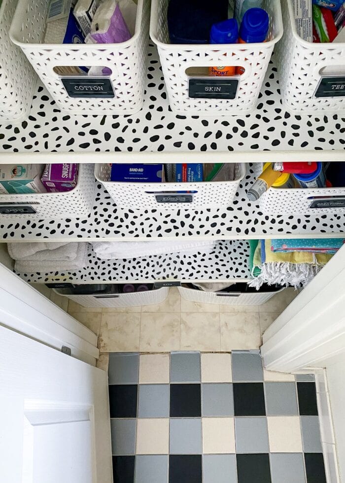 Black and white organized bathroom closet shown against plaid tile floors