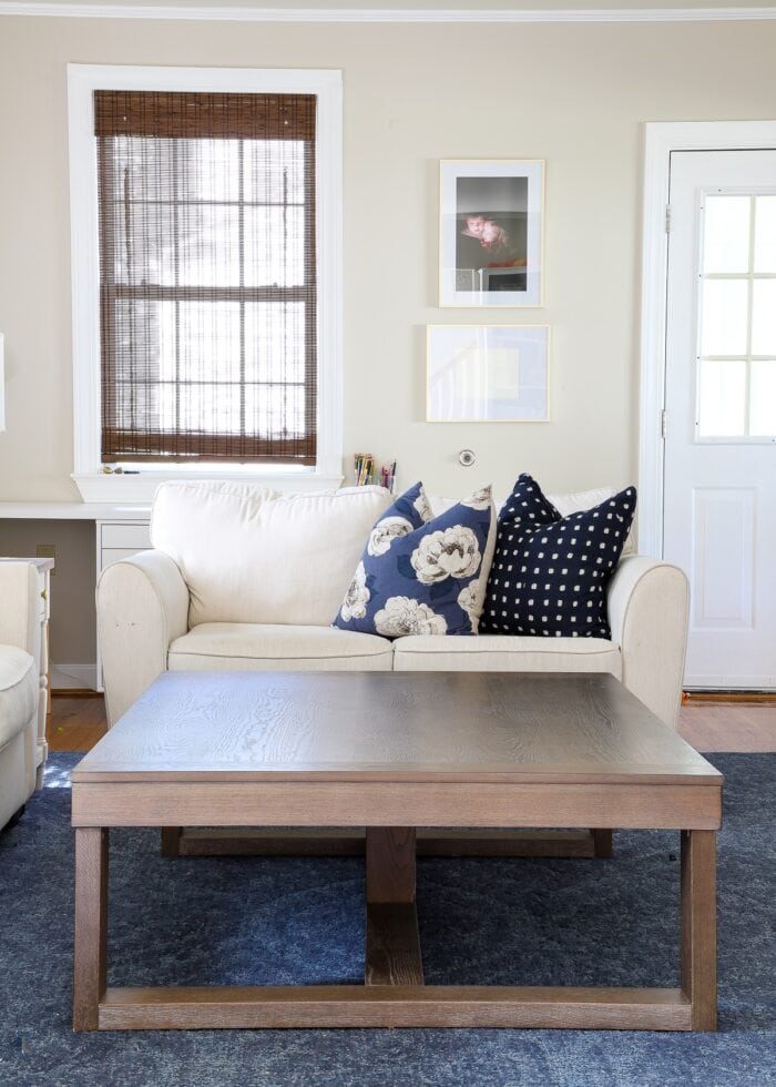 Large wooden coffee table in front of a white love seat with blue throw pillows