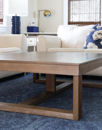 Large coffee table in front of white couches on top of blue rug