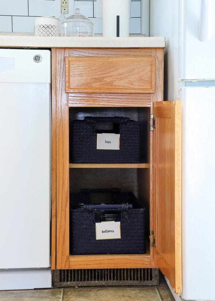 Blue baskets holding food storage containers in an oak kitchen cabinet