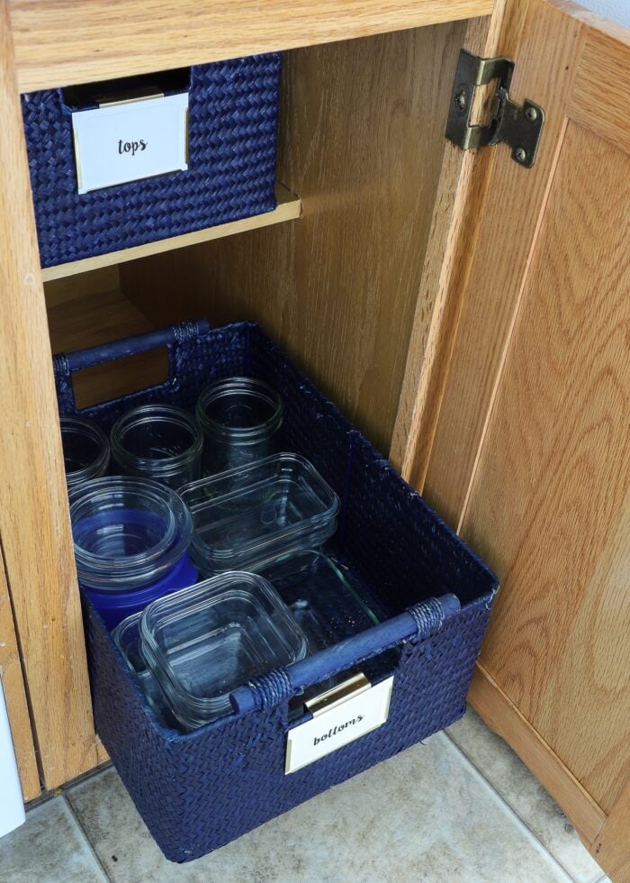 Food storage containers in a blue basket inside a skinny oak kitchen cabinet