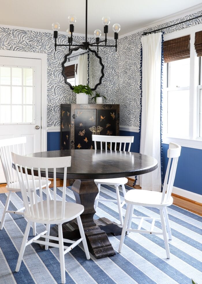 White dining room chairs at a dark table on top of a blue striped rug