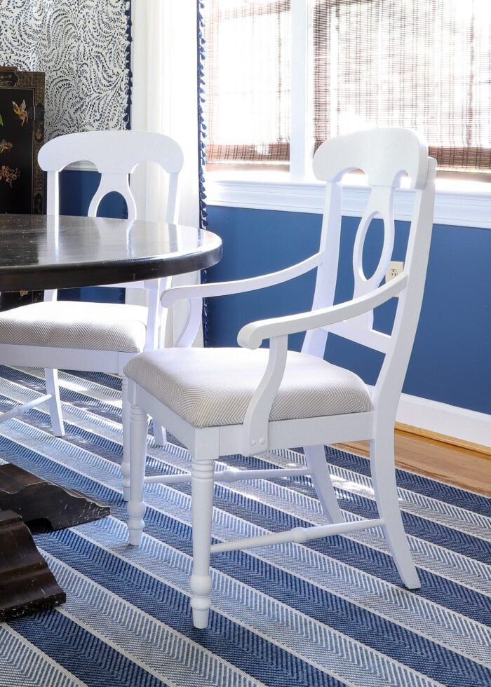 White wooden dining room chairs at a dark table on top of a blue striped rug