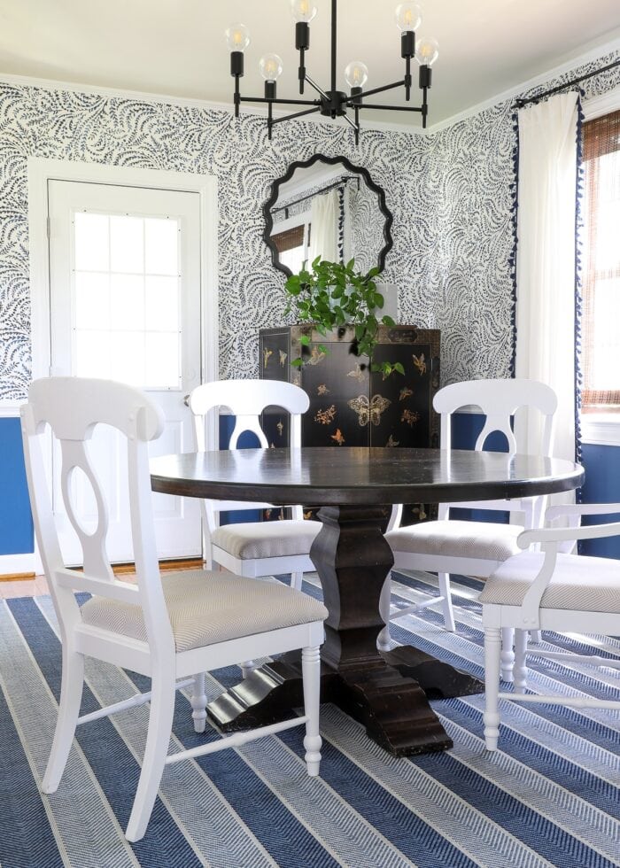 White wooden dining room chairs at a dark table on top of a blue striped rug