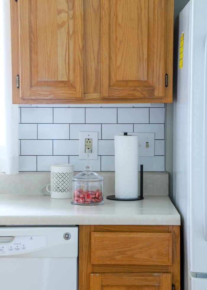 Builder-grade rental kitchen with honey oak cabinets and white peel and stick subway tile on the backsplash