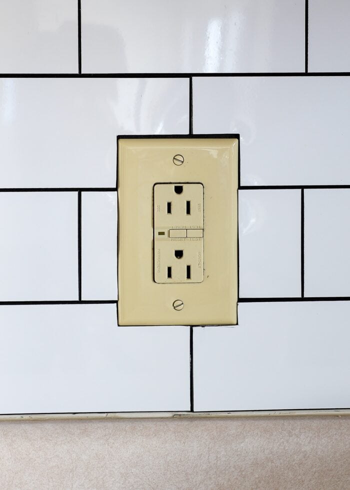 Tan outlet cover surrounded by white peel and stick subway tile