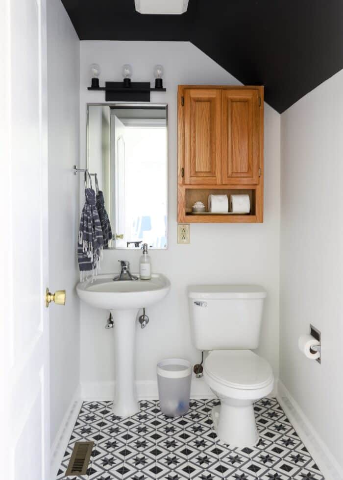 Modern black and white rental bathroom with oak cabinet above toilet