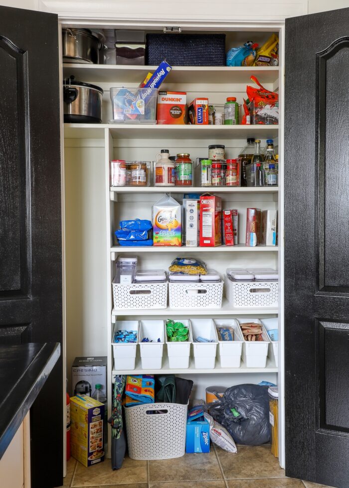 Pantry with black doors, wooden shelves, and some bins and baskets holding a mess of foods