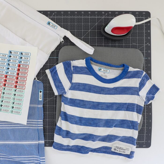 A blue and white striped shirt shown next to a sheet of iron on labels on top of a Cricut cutting mat