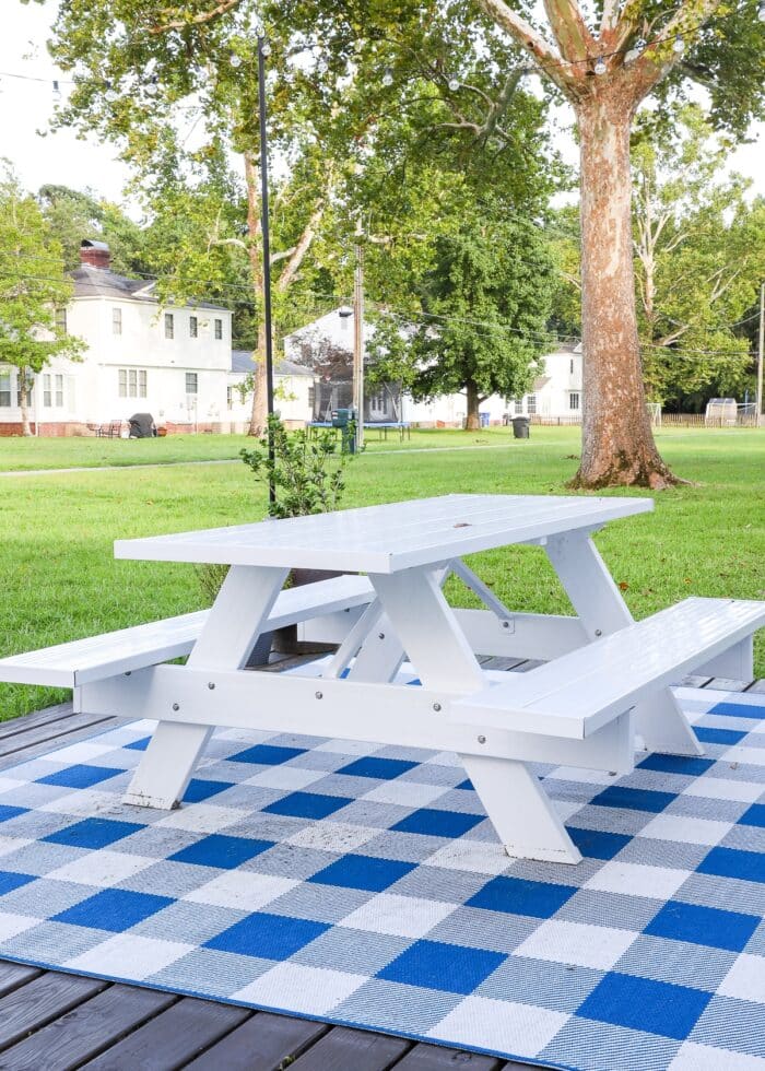 Blue and white checked rug, white picnic table on a white and wood deck