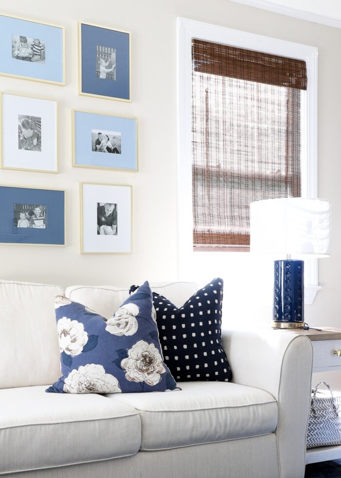White couch next to a white side table with blue lamp, pillows, and artwork