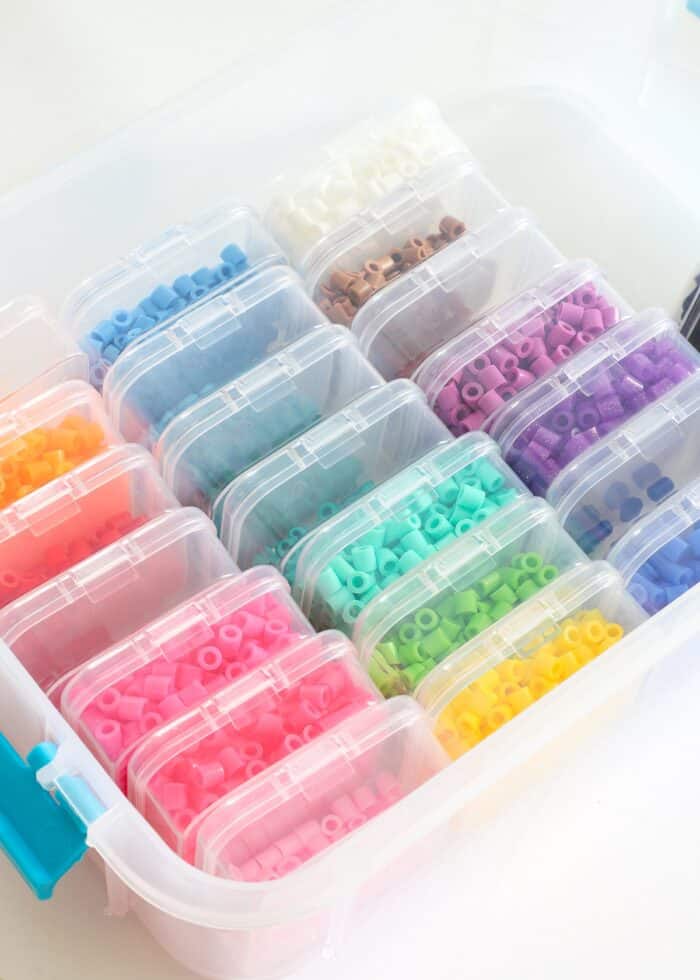 Perler beads sorted by rainbow colors into small plastic bead boxes inside a tiered organizer