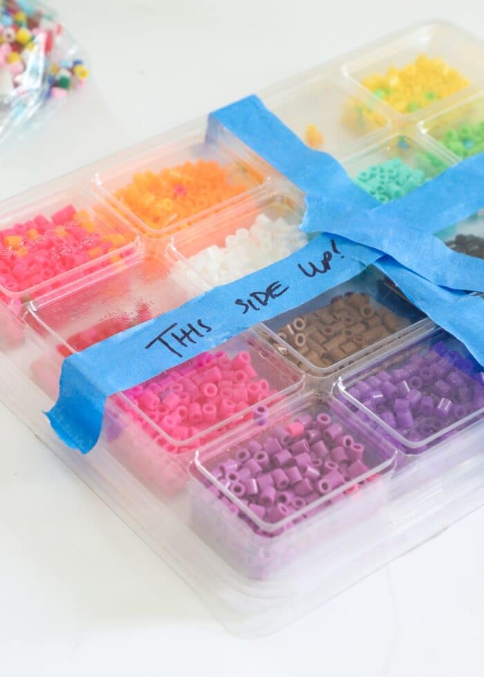 Perler beads in a plastic sorter with blue tape saying "This Side Up"