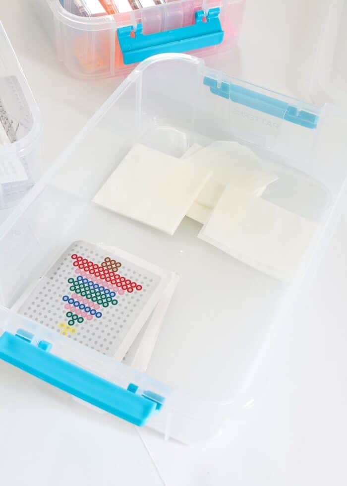 Perler bead patterns and papers loaded into a tiered plastic box for storage